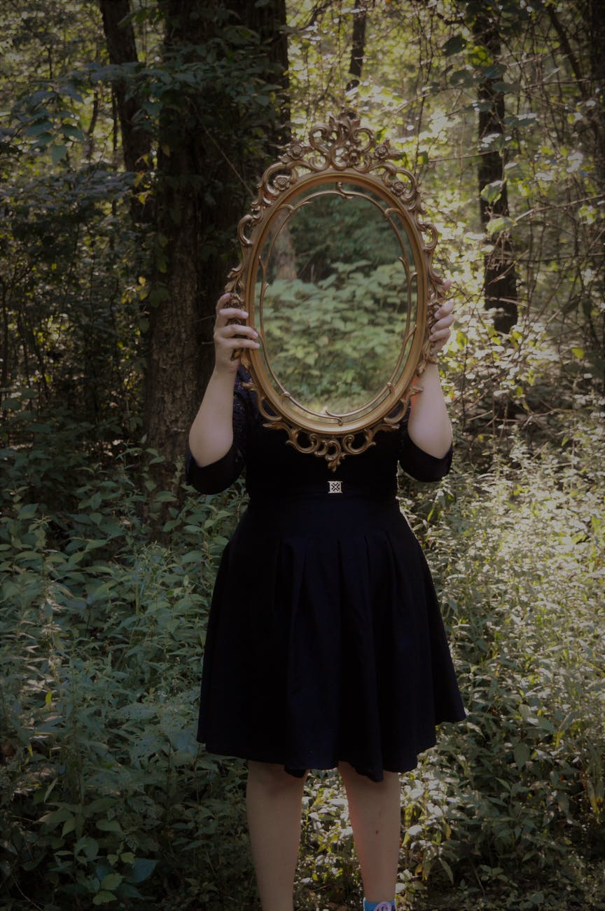 girl holding mirror over face in forest