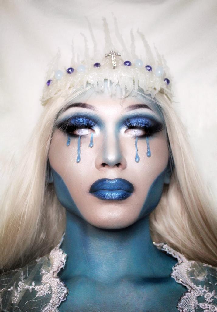Woman with white hair and blue make-up and blue tears against white background