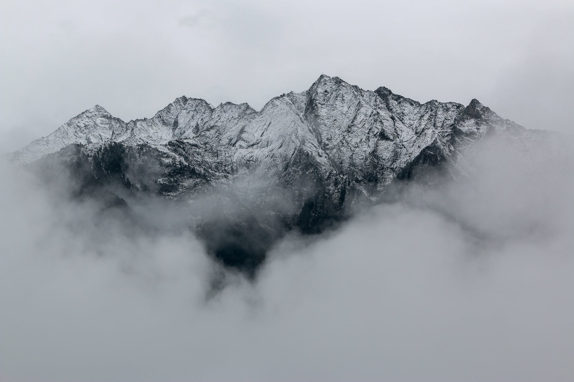 Snow covered mountain with light background with clouds around the top of the mountain. 